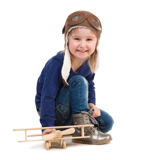 Cute little girl in pilot hat with wooden plane