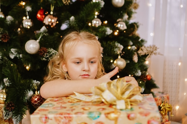 Cute little girl in pink dress with present on background Christmas tree