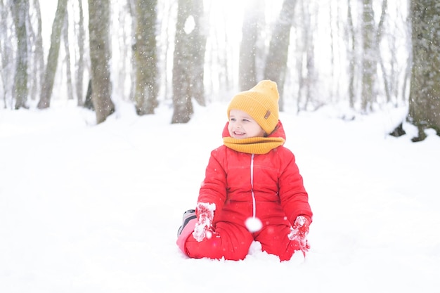 Cute little girl in pink snowsuit plays with snow in winter forest