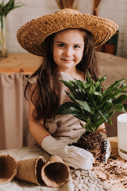 A cute little girl plants and waters a flower in a pot at home A little summer resident takes care of home flowers Earth Day