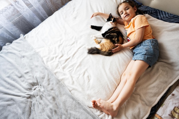 Cute little girl playing with her cat on the bed at home