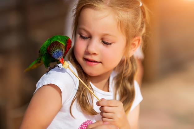 Cute little girl playing with a parrot and feed him