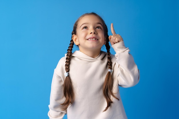 Cute little girl pointing up and having idea against blue background