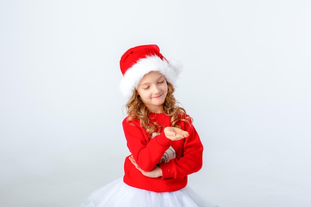 cute little girl in a red sweater and Santa hat on a white background. Christmas concept, text space