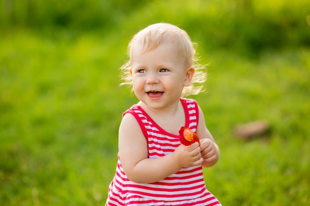 Cute little girl smiling in red summer dress walking on green lawn