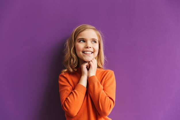 Cute little girl standing isolated over violet wall, looking away