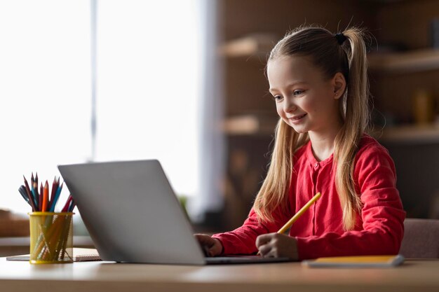 Cute little girl study with laptop at home and writing in notepad