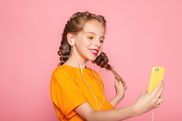 Cute little girl taking selfie. Photo of cute lovely small lady long telephone show thumb-up make selfie toothy beaming smile wear casual stylish red t-shirt isolated pink color wall