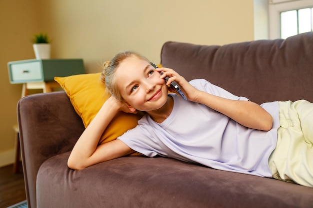 Cute little girl useing smartphone and lying down on sofa in viving room at her home