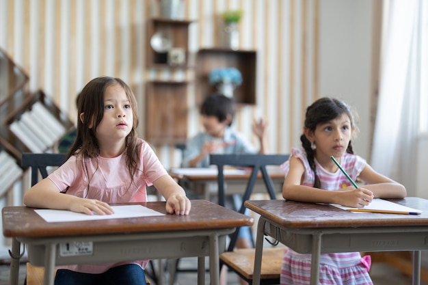 Cute little girl using color pencil drawing on paper in art study class at elementary school