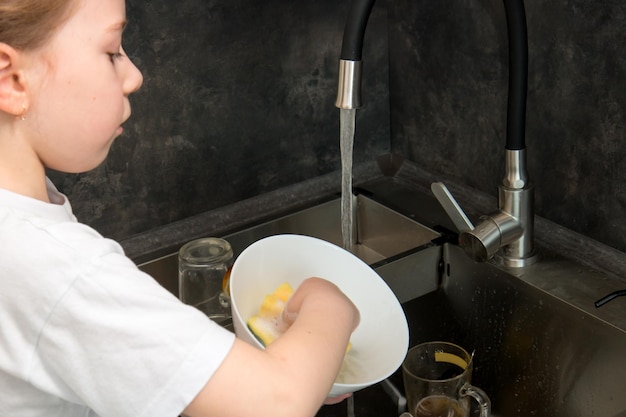 Cute little girl washing dishes in the kitchen by the sink