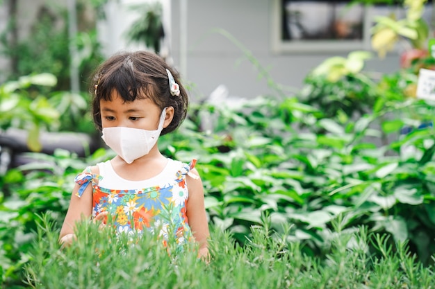 Cute little girl wearing protective face mask looking at rosemary plant