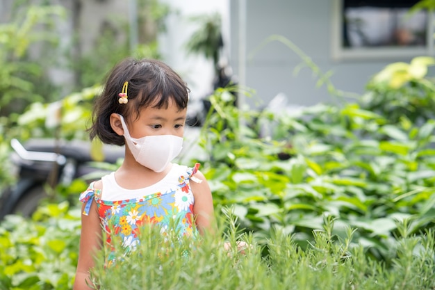 Cute little girl wearing protective face mask looking at rosemary plant