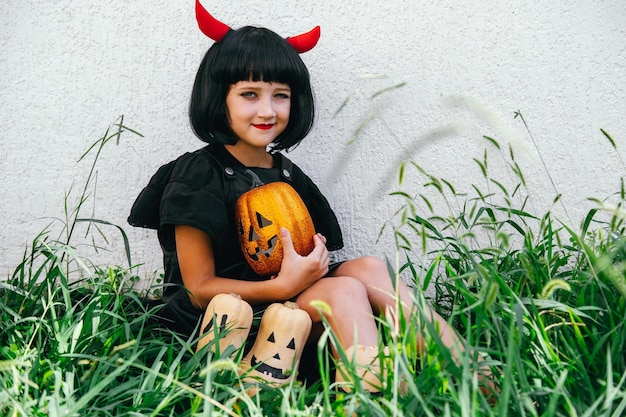 Cute little girl wearing wig with red horns holding pumpkin Halloween celebration party portrait