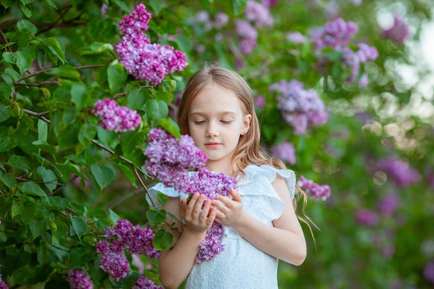 cute little girl in a white dress in a blooming lilac spring garden