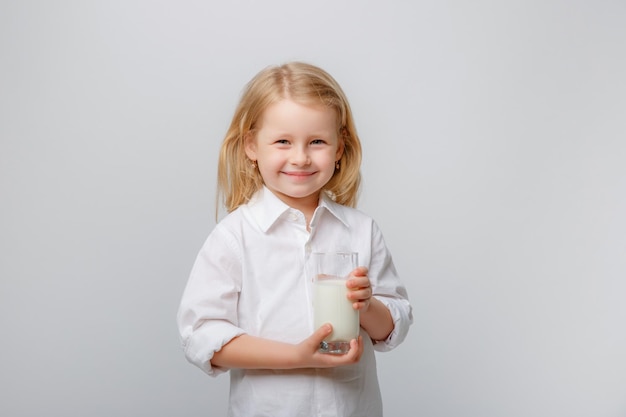 Cute little girl in a white shirt holding a glass of milk on a white background