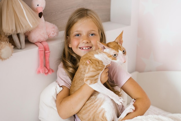 Cute little girl with cat sitting on bed at home