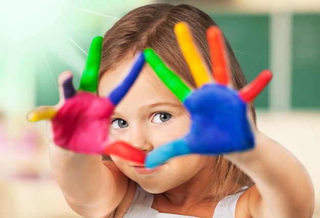 Cute little girl with colorful painted hands on class background