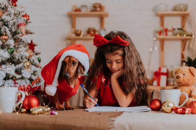 Cute little girl with a dwarf dachshund writes letter with wishes to Santa Claus christmas concept