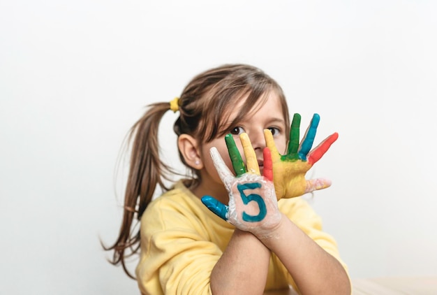 Cute little girl with the five number painted on the hand looking at camera Little girl who is painting her hands with numbers The number five leisure activity and childhood concept