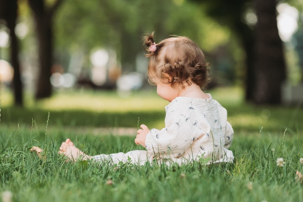 cute little girl with a funny hairstyle is sitting on a blooming green lawn in the park Lifestyle