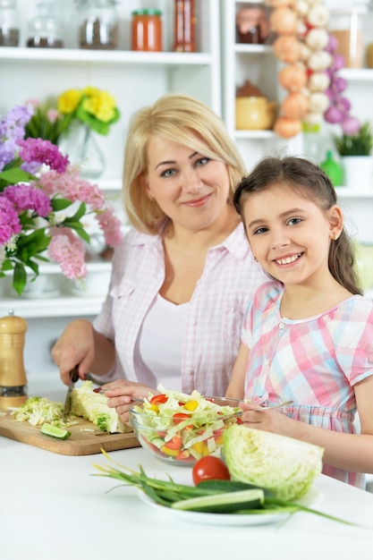 Cute little girl with her mother cooking together at kitchen table