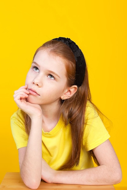 A cute little girl with long brown hair in a yellow Tshirt is standing in the studio on a yellow background Isolate Childhood games classes school hobbies