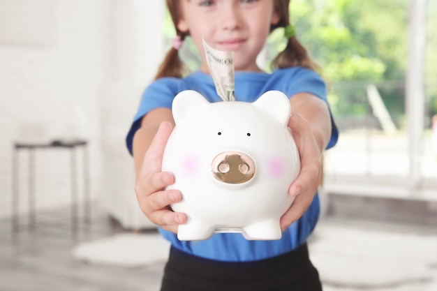 Cute little girl with piggy bank indoors