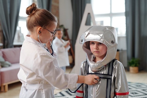 Cute little girl with stethoscope examining astronaut in space-suit