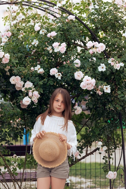 Cute little girl with a straw hat for a bush of white roses