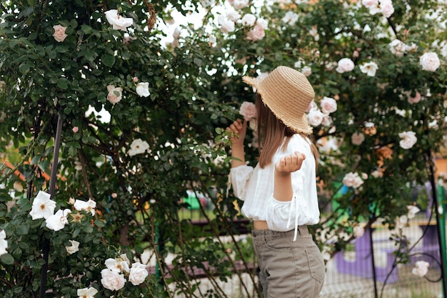 Cute little girl with a straw hat for a bush of white roses