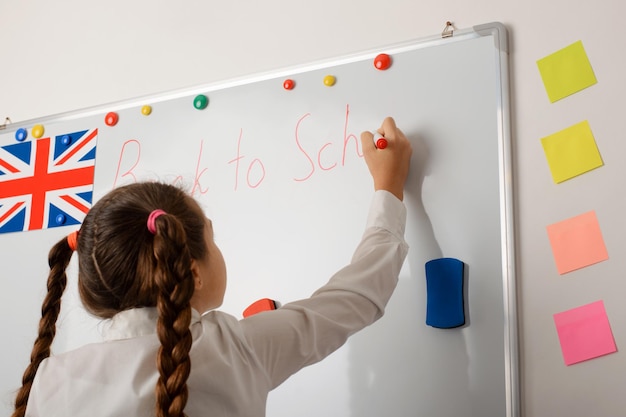 Cute little girl writing on blackboard Back to school inscription