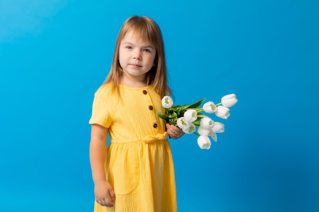 A cute little girl in a yellow cotton dress with a bouquet of tulips on a blue background March 8 mother39s day banner space for text