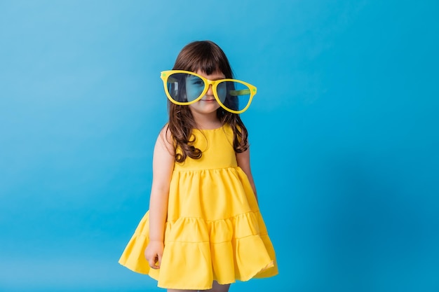 Cute little girl in a yellow dress and huge sunglasses stands on a blue background card banner