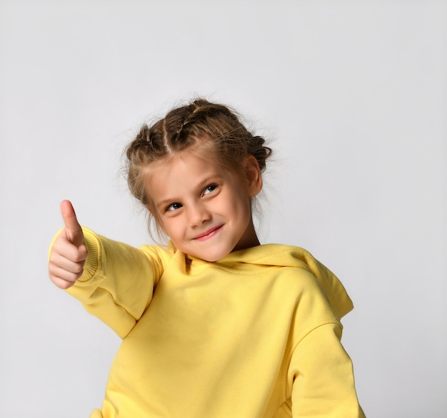 Cute little girl in a yellow hoodie waistlength portrait showing thumb up