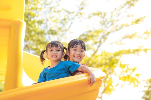 Cute little girls siblings having fun on playground outdoors on sunny summer day. Children on plastic slide. Fun activity for kid. active sport leisure for kids