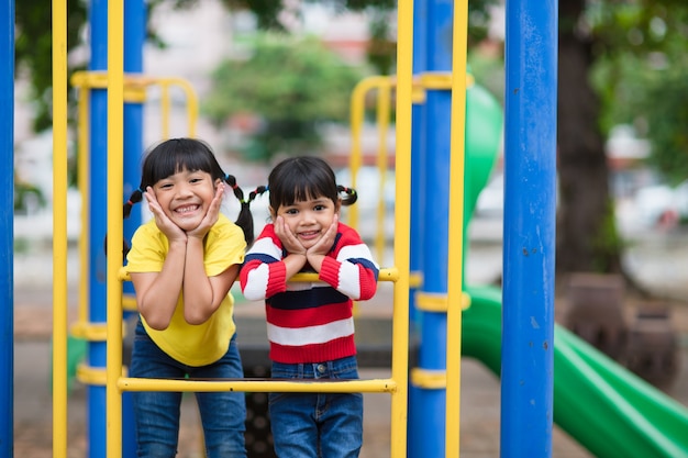 Cute little girls siblings having fun on playground outdoors on sunny summer day