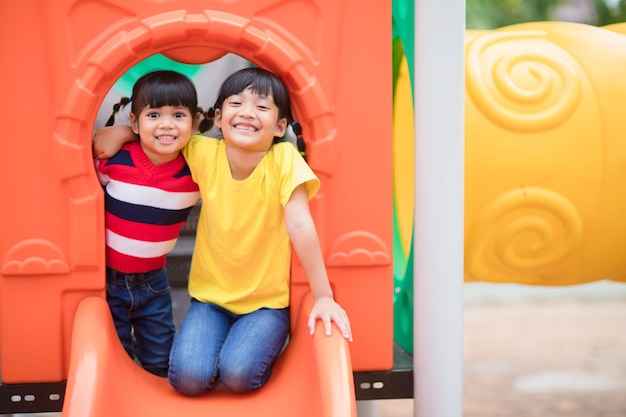 Cute little girls siblings having fun on playground outdoors on sunny summer day