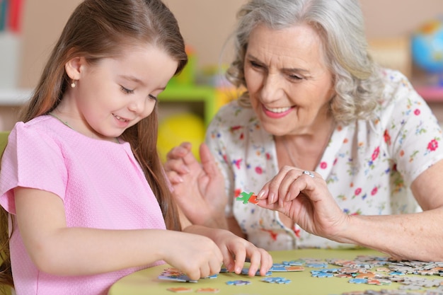 Cute little granddaughter and grandmother collecting puzzles