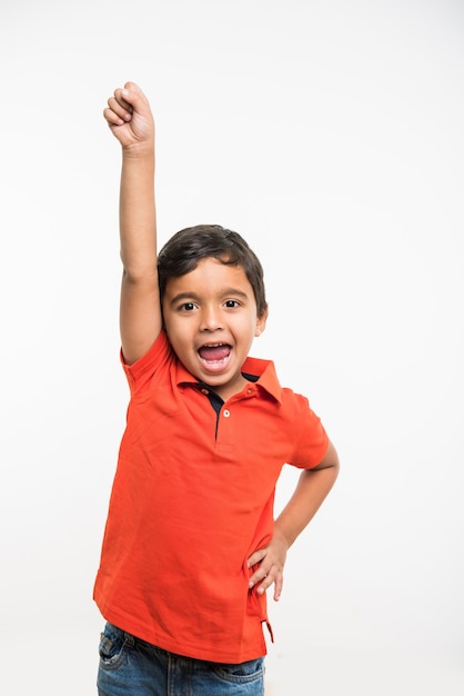 Cute little indian asian boy with hands stretched, holding book, magnifying glass or victory trophy, standing isolated over white background