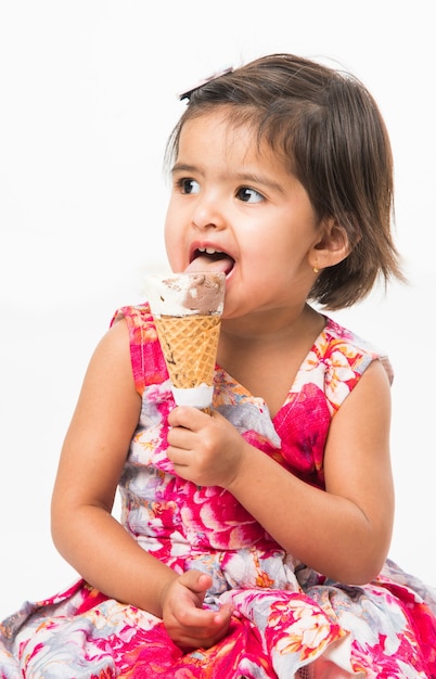 Cute little indian asian girl child licking or eating chocolate ice cream in cone, isolated over white background