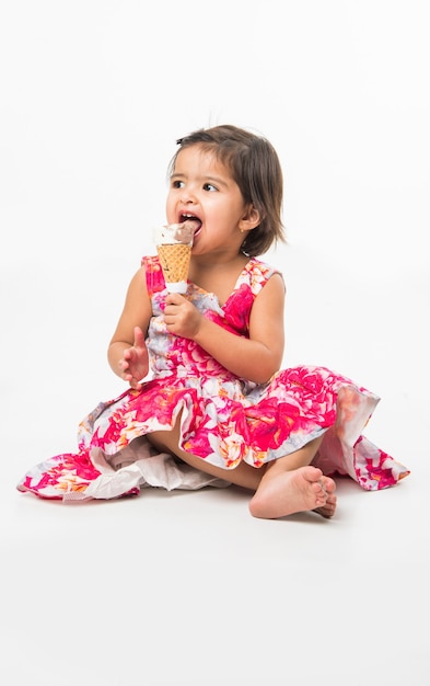 Cute little indian asian girl child licking or eating chocolate ice cream in cone, isolated over white background