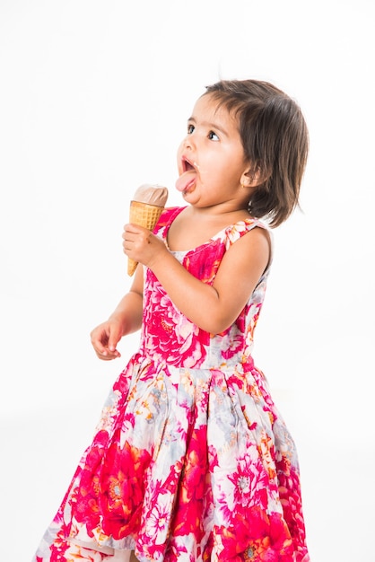 Cute little indian asian girl child licking or eating chocolate ice cream in cone, isolated over white background