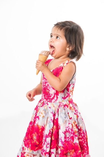 Cute little indian asian girl child licking or eating chocolate ice cream in cone, isolated over white background