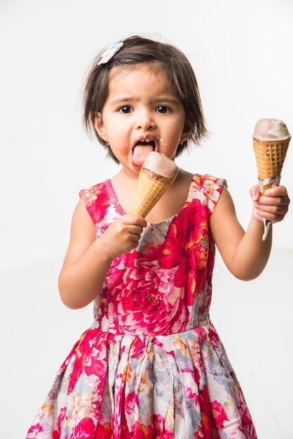 Cute little indian asian girl child licking or eating chocolate ice cream in cone, isolated over white background