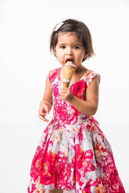 Cute little indian asian girl child licking or eating chocolate ice cream in cone, isolated over white background