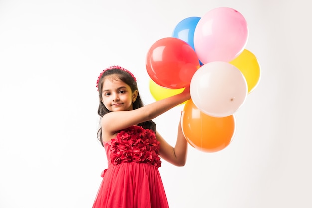 Cute little indian or asian girl with colourful balloons or gubbare in Hindi, over white or red background