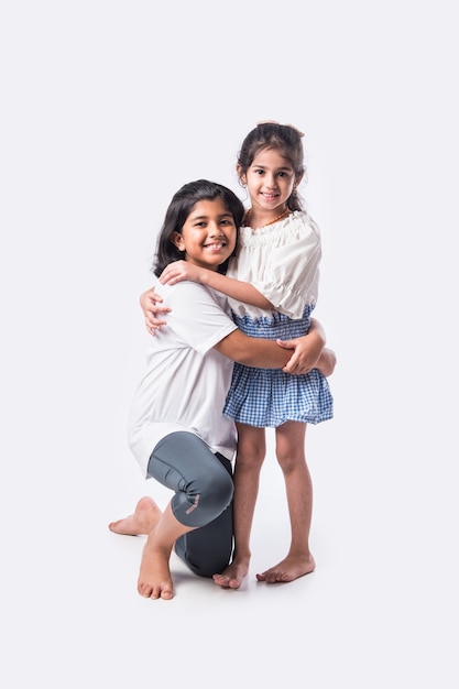 Cute little Indian asian siblings standing and embracing each other in white clothes while standing againstwhite background.