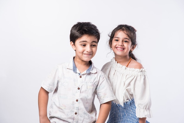 Cute little Indian asian siblings standing and embracing each other in white clothes while standing againstwhite background.