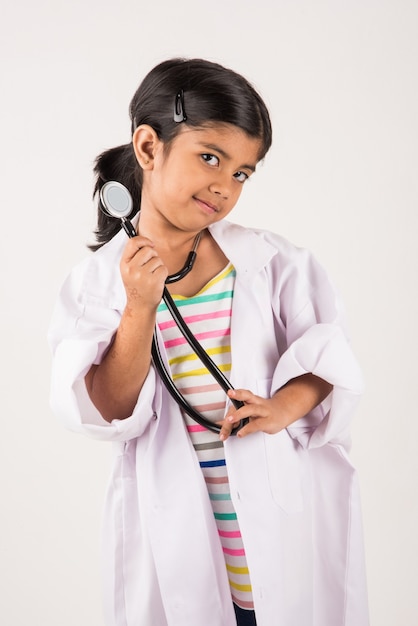 Cute Little Indian girl doctor with stethoscope while wearing Doctor's uniform. Standing isolated over white background